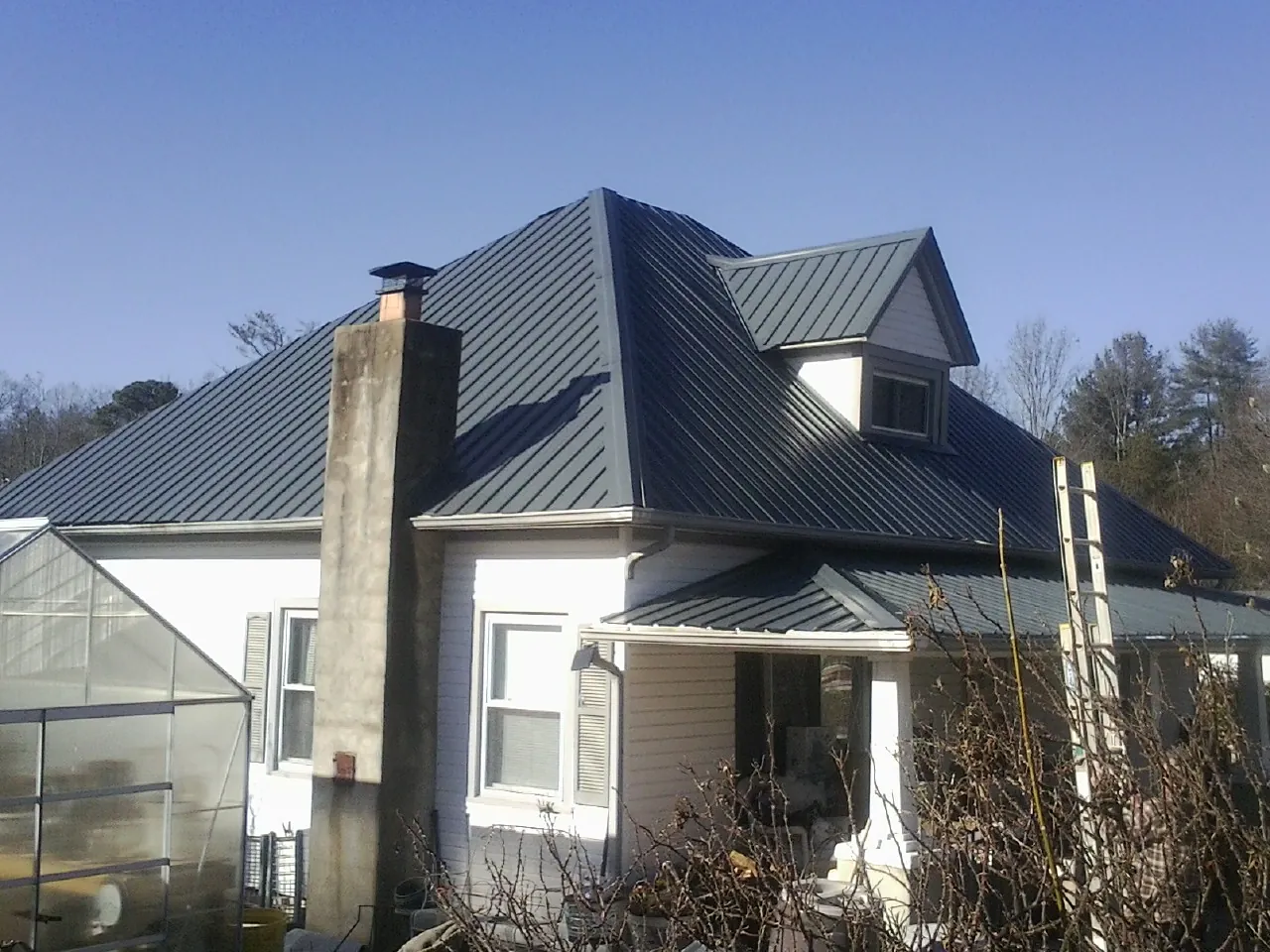 Dark blue standing seam metal roof on a white farmhouse with dormer — Slate & Tile Roof Repair by Roofing Brothers in Preston Hollow
