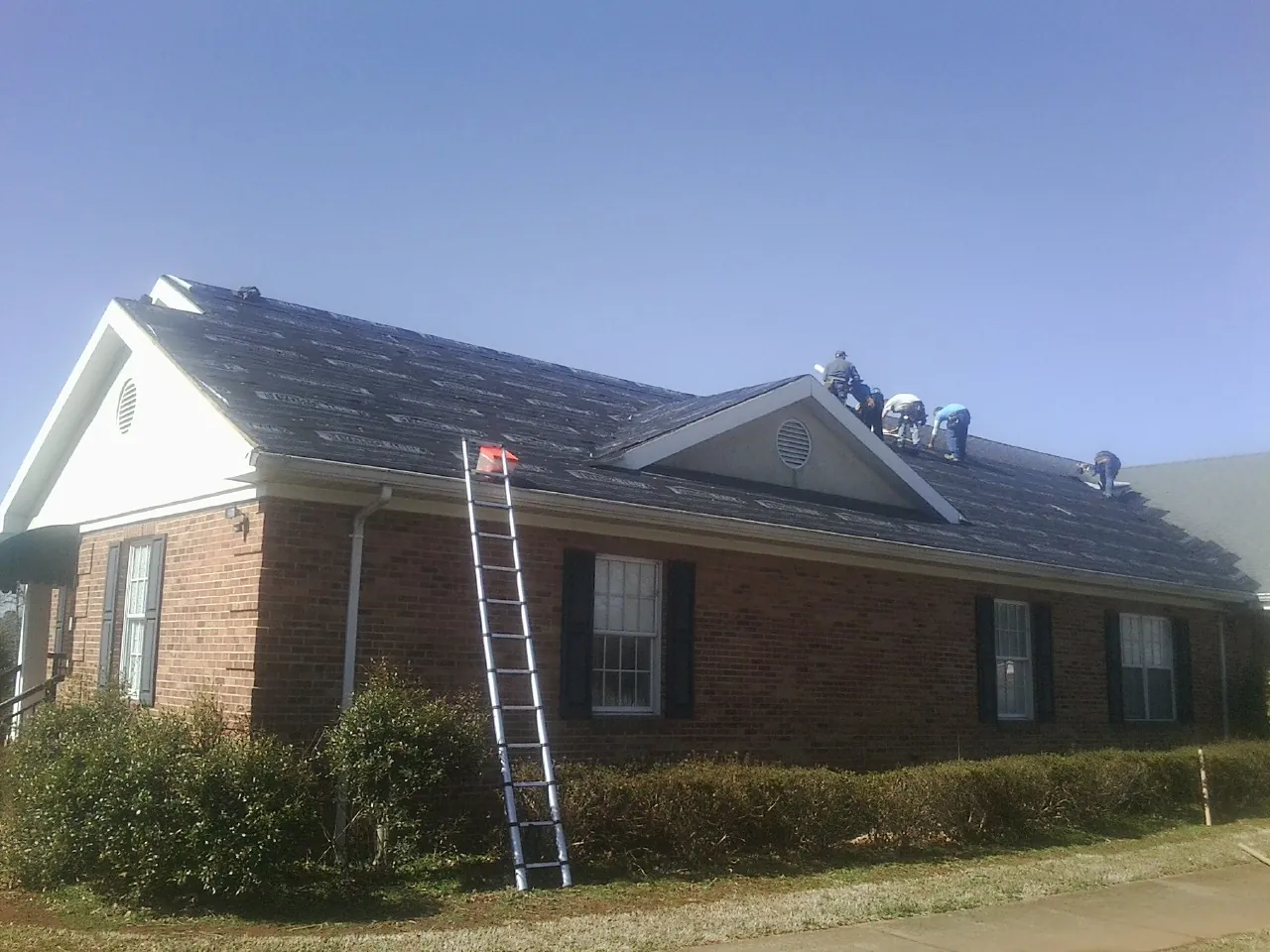 Crew tearing shingles off a brick ranch roof with a ladder set — Emergency Roof Repair work by our crew in Preston Hollow