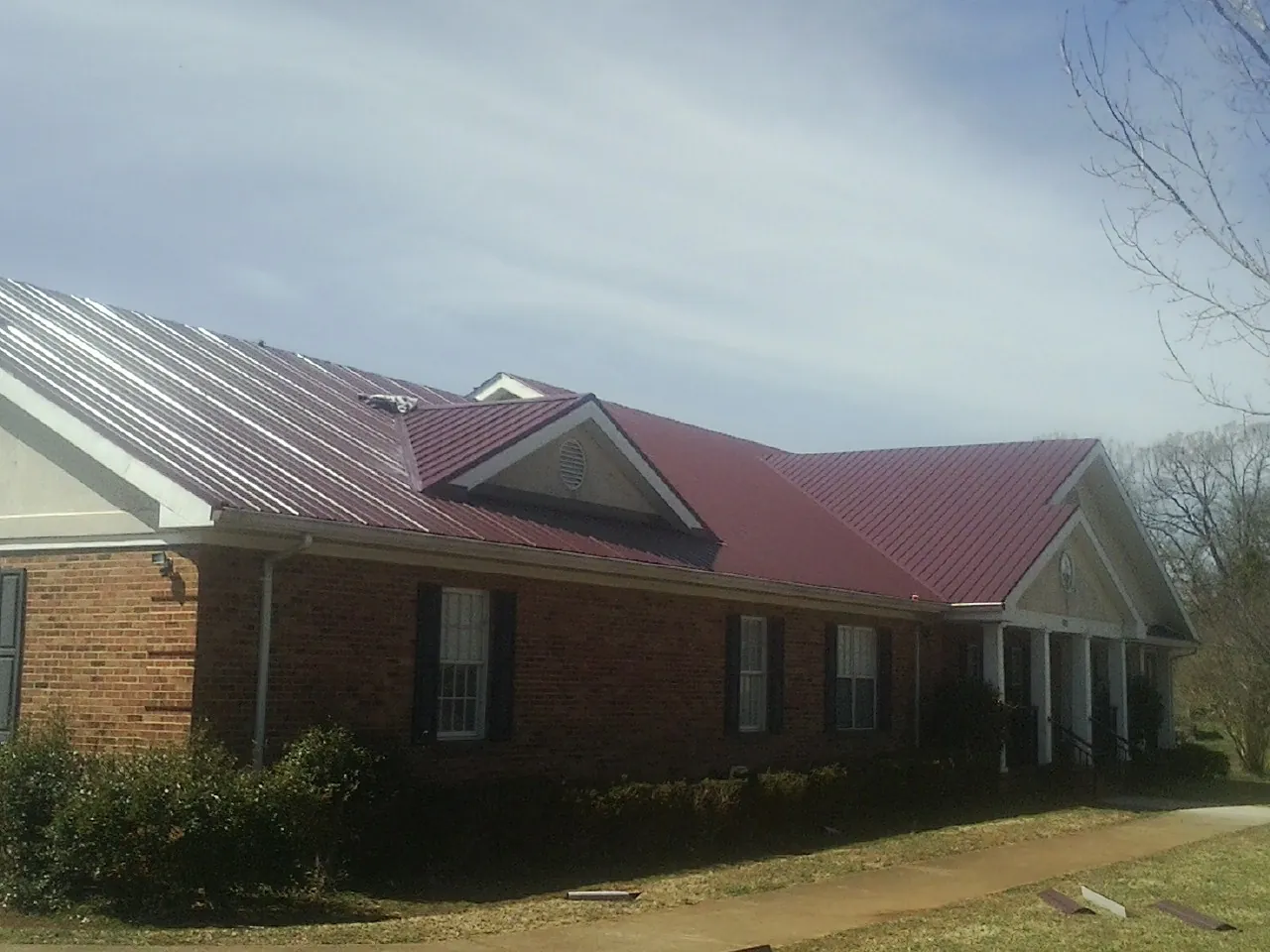 Red metal roof with gabled entries on a long brick building, from a Hail Damage Roof Repair job in Preston Hollow