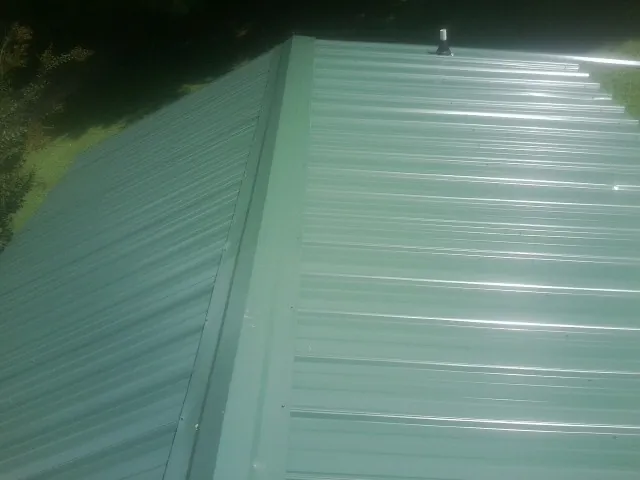 New green metal panels meeting at the ridge of a roof — Flat Roof Repair work by our crew in Preston Hollow