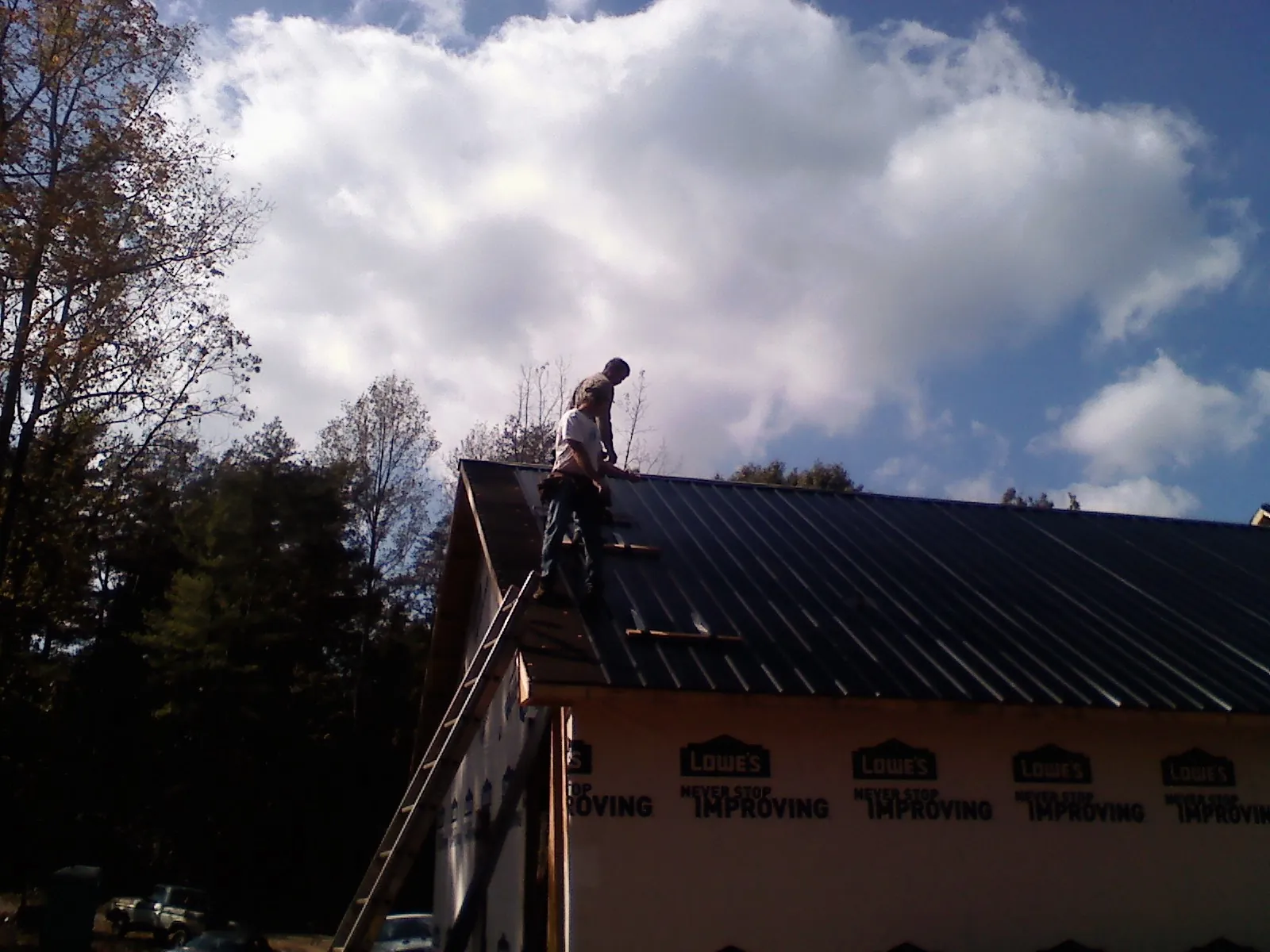 Roofer fastening dark metal panels high against a cloudy sky, from a Roof Inspection job in Preston Hollow