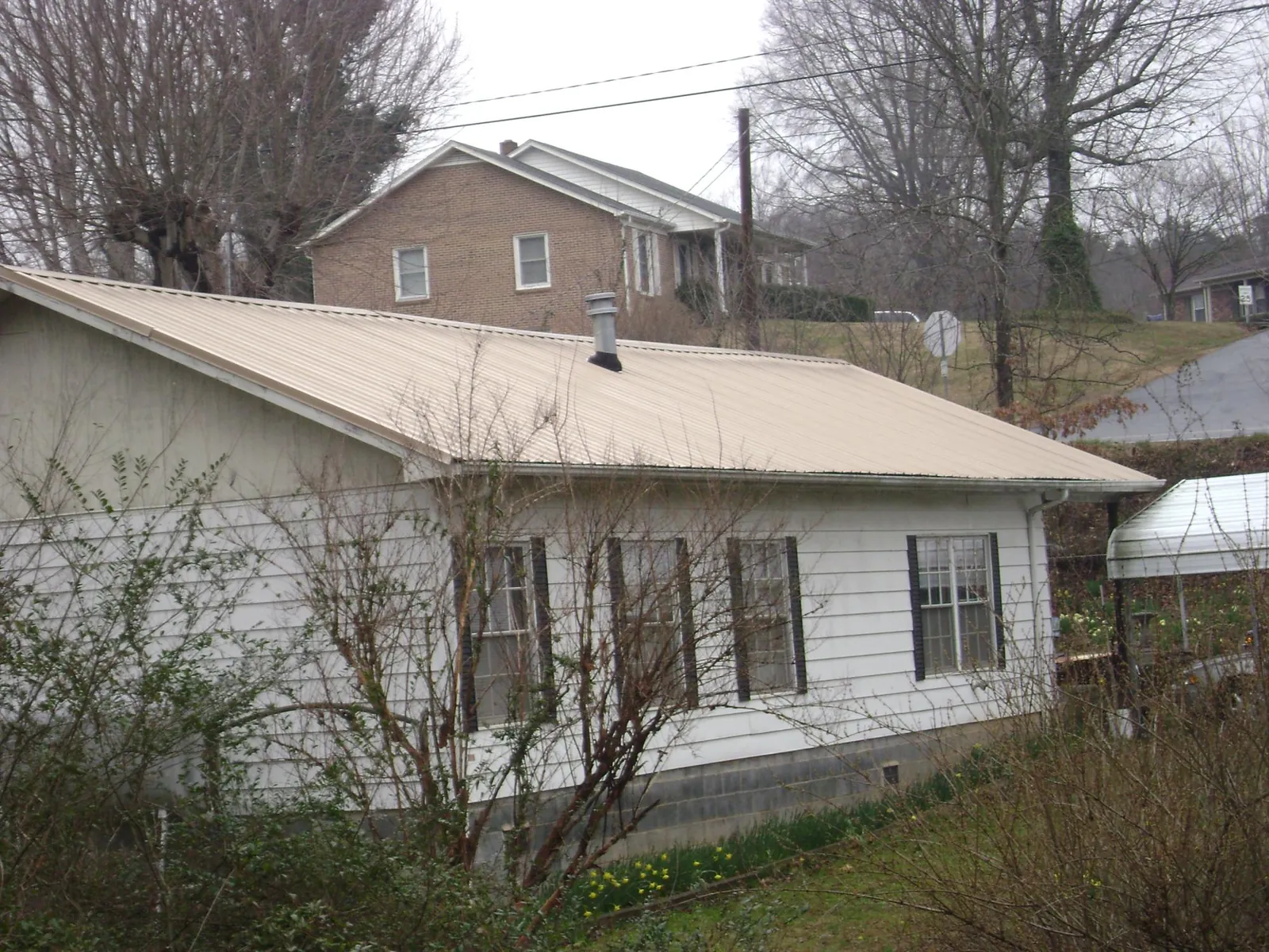 Tan metal roof on a white sided house set into a hillside — Commercial Roofing by Roofing Brothers in Preston Hollow