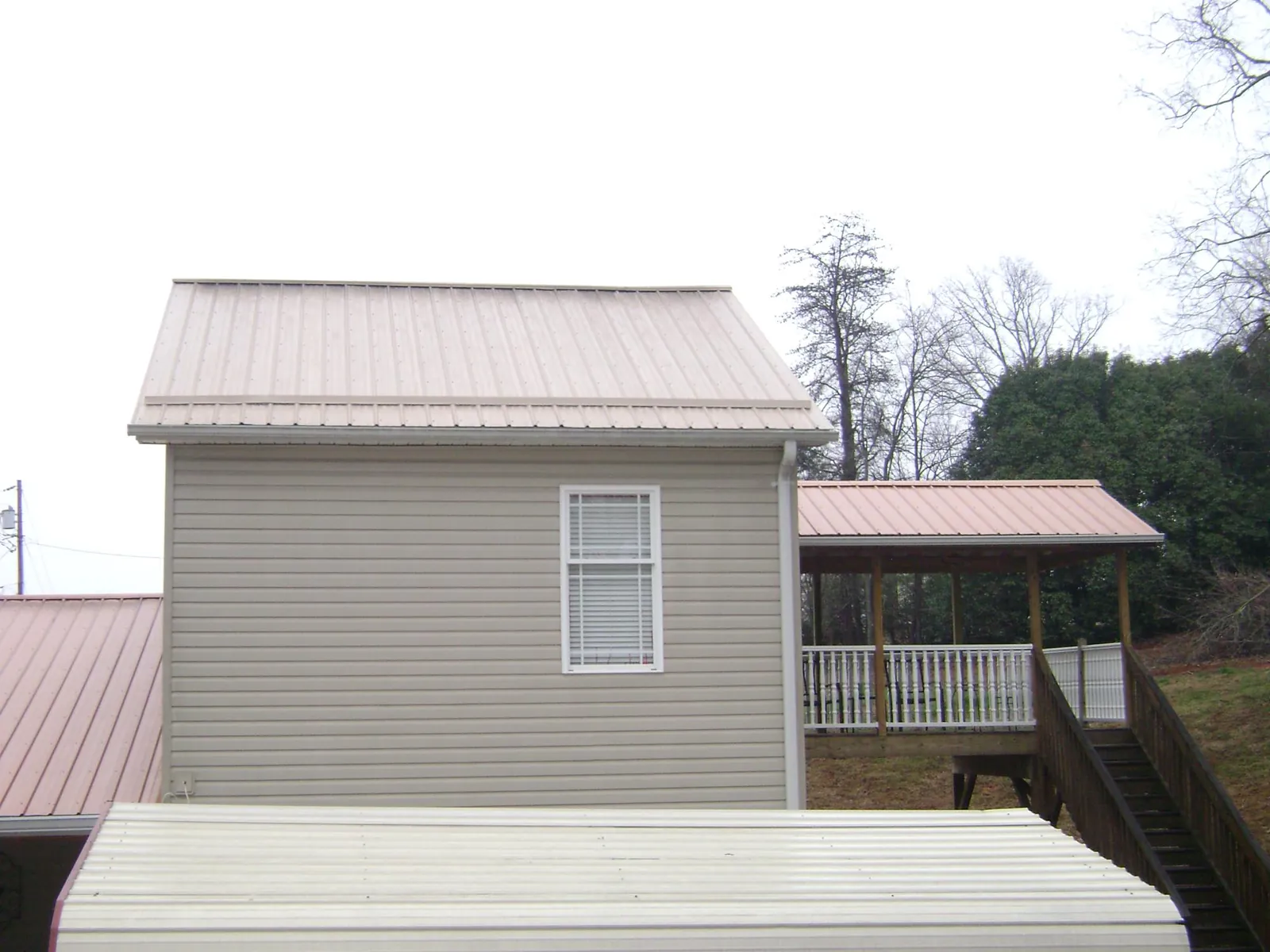 Tan metal roofs on a two story addition and attached porch, from a Roof Replacement job in Preston Hollow